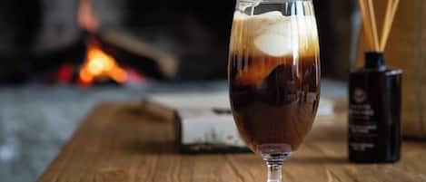 A glass of iced coffee on a wooden table with a candle and reed diffuser in the background.