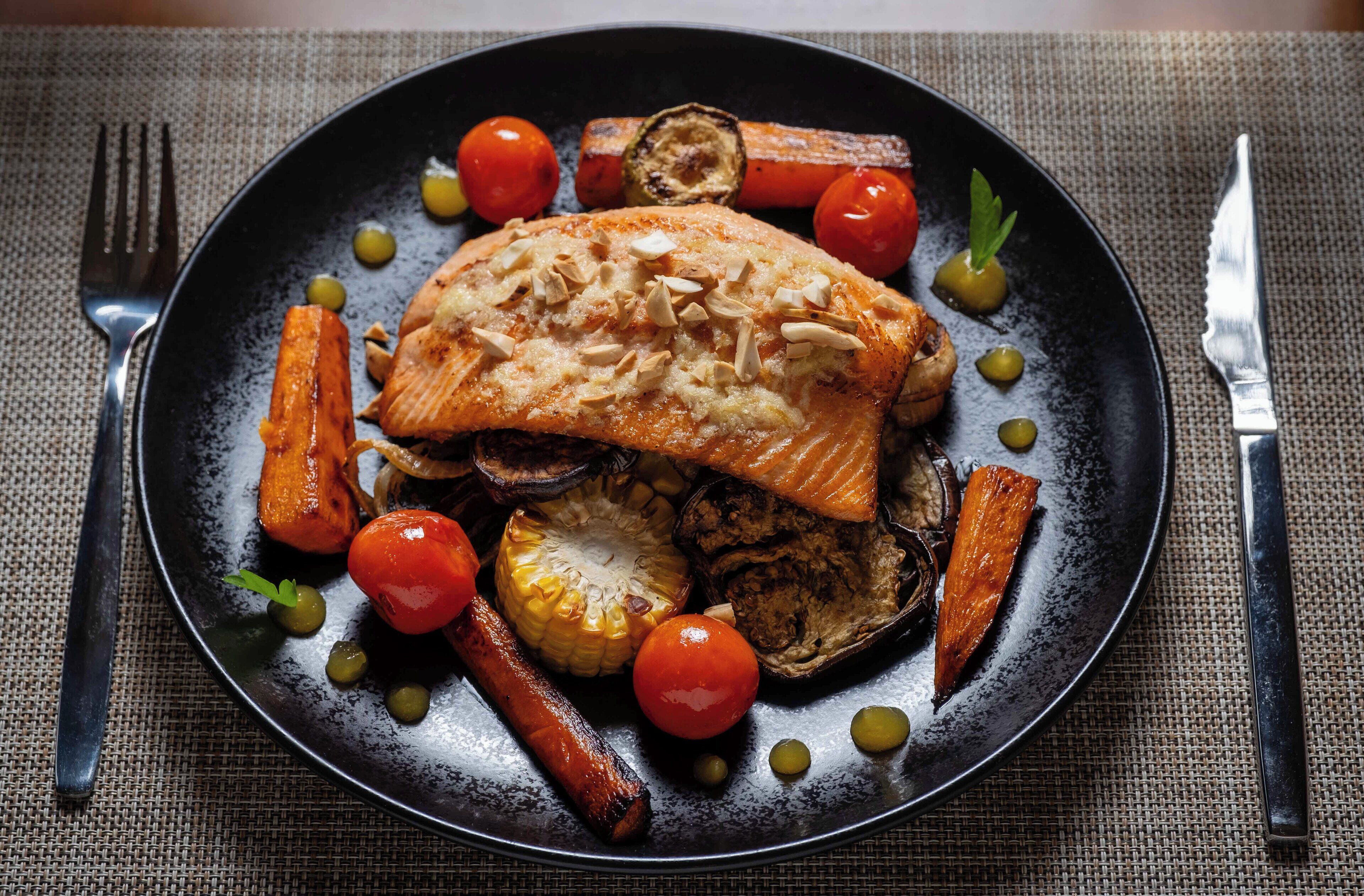 Une assiette de nourriture contenant du saumon, des carottes et des tomates.
