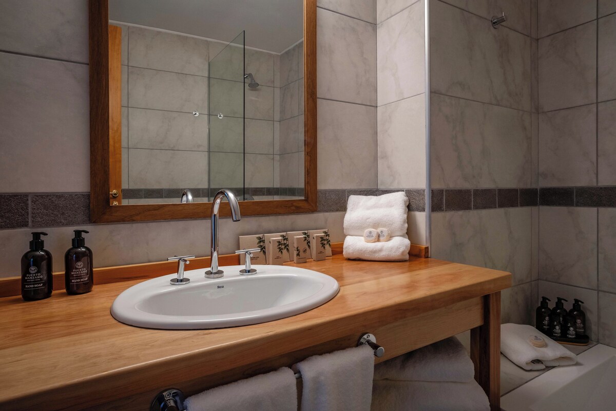 Un baño con tocador de madera, lavabo blanco, espejo y zona de ducha.