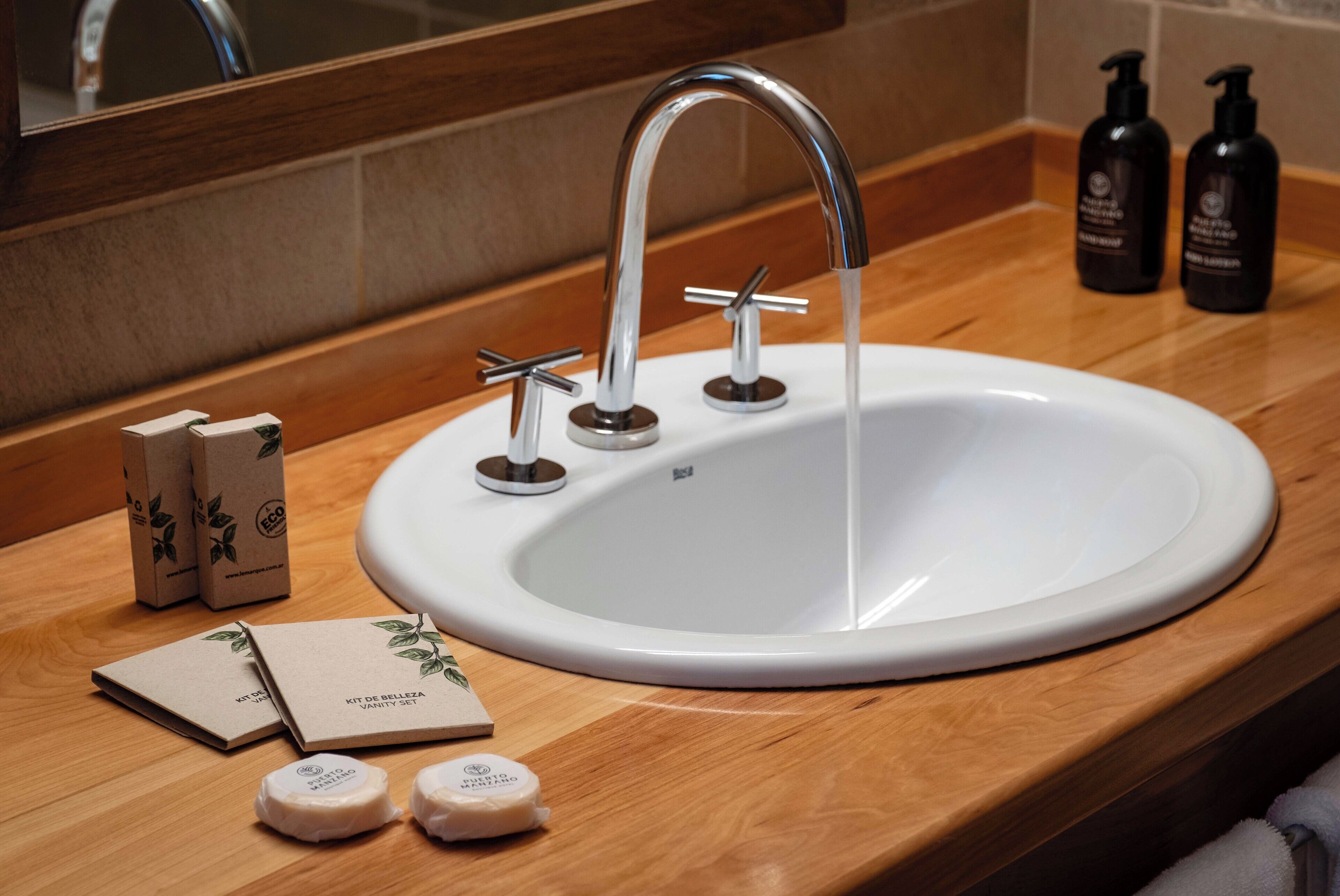 A white sink with a modern faucet, two soap dispensers, and two bottles of hand soap on a wooden countertop.