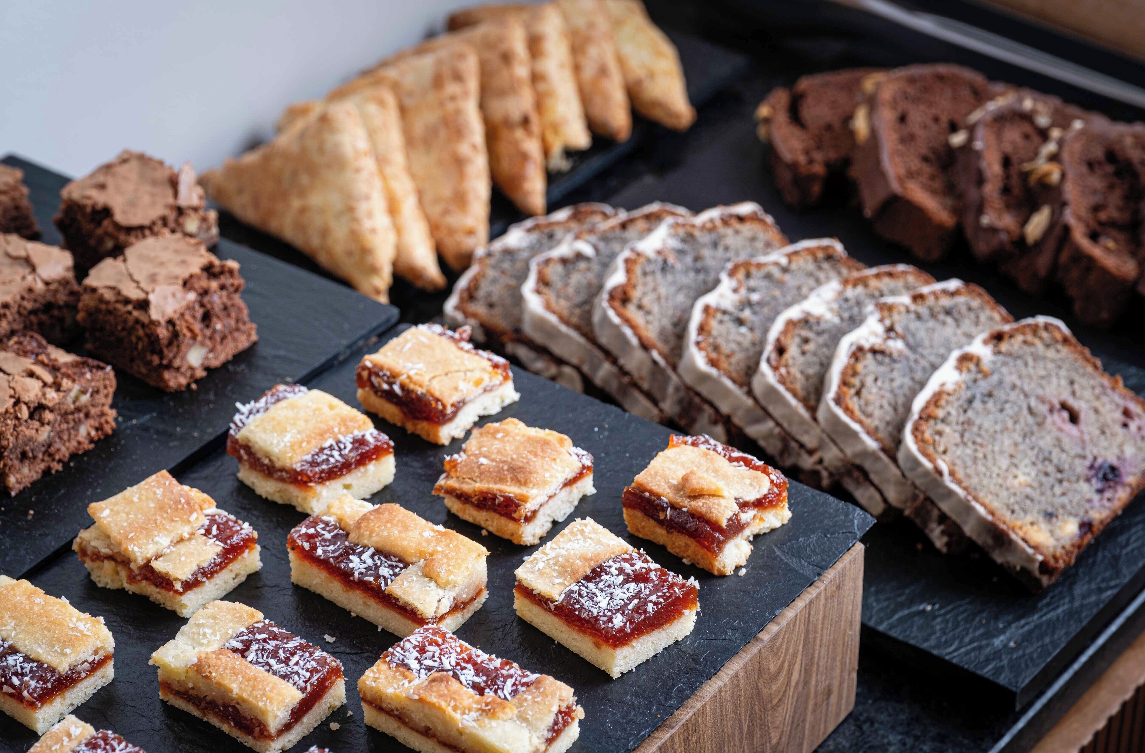 Une variété de produits de boulangerie, notamment des brownies, des carrés recouverts de confiture et des tranches de pain.