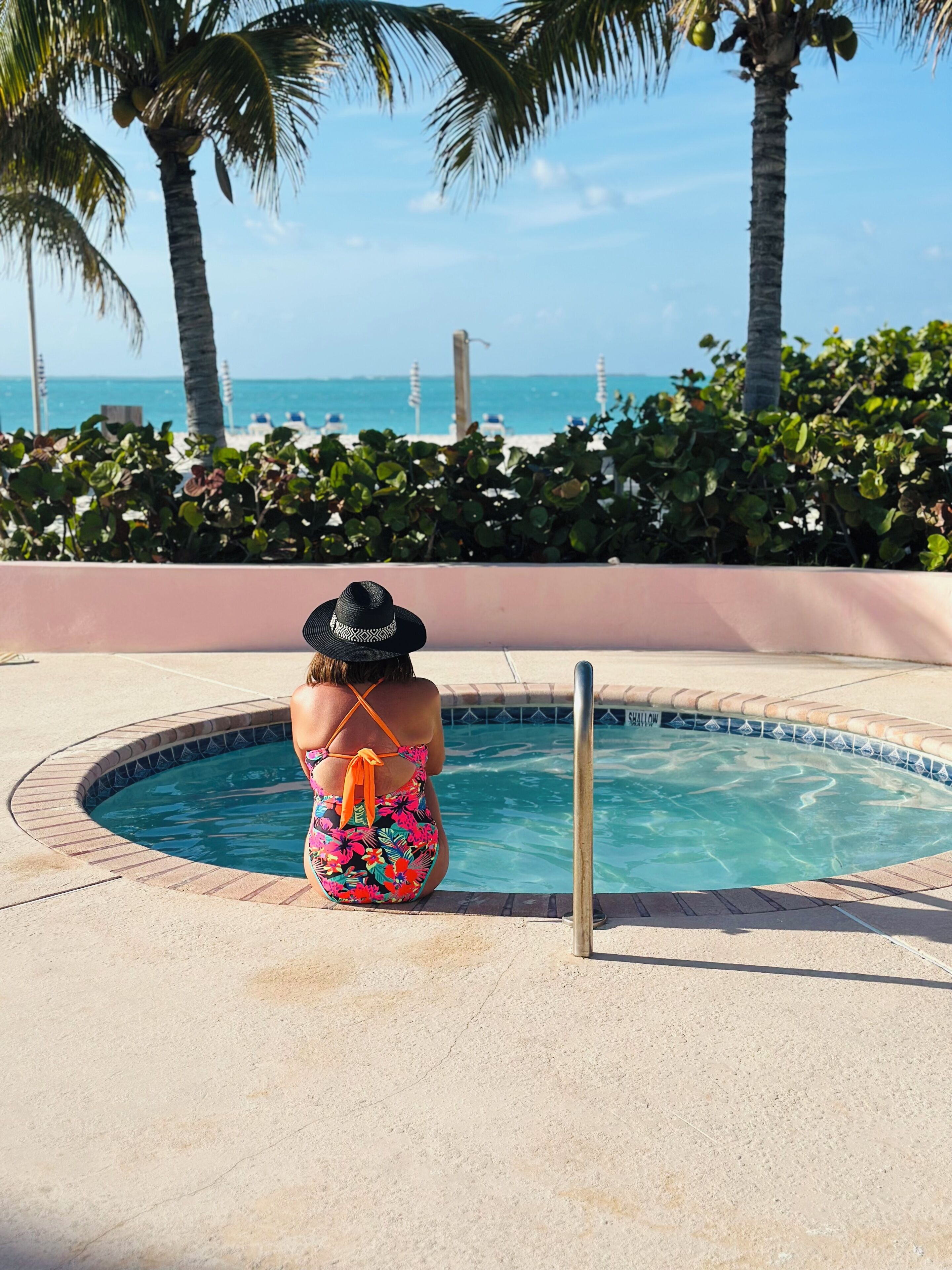 A person sitting by a pool with a view of the ocean and palm trees.