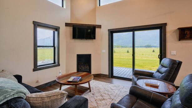 A spacious living room with a fireplace, leather sofas, a coffee table, and large windows offering a view of a green landscape.
