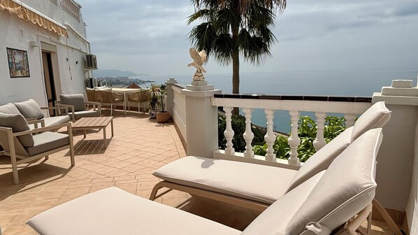 A terrace with white furniture, a statue, and a view of the sea.