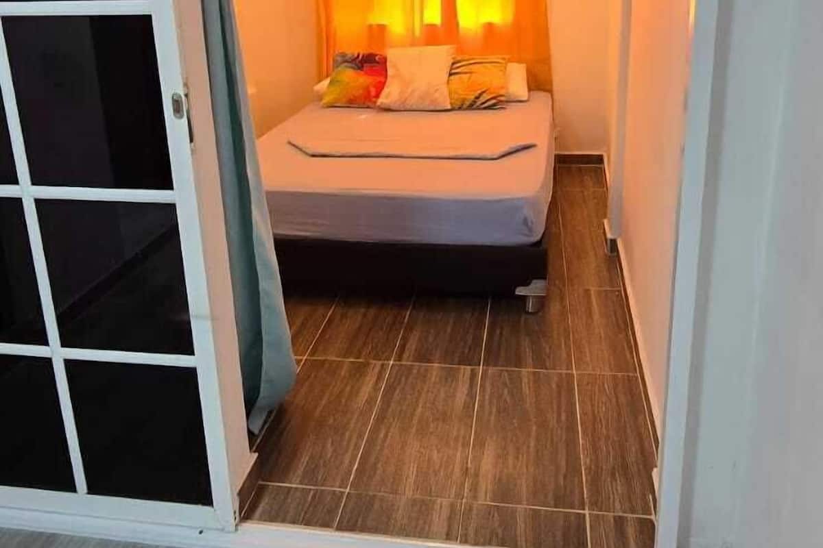 A small bedroom with a bed, a sliding door, and a ceiling-mounted air conditioning unit.
