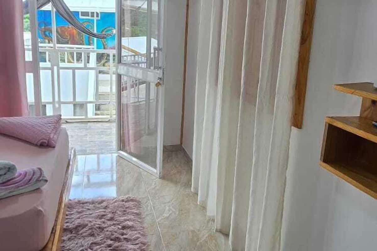 A room with a bed, a TV mounted on the wall, a window with curtains, and a view of a building outside.