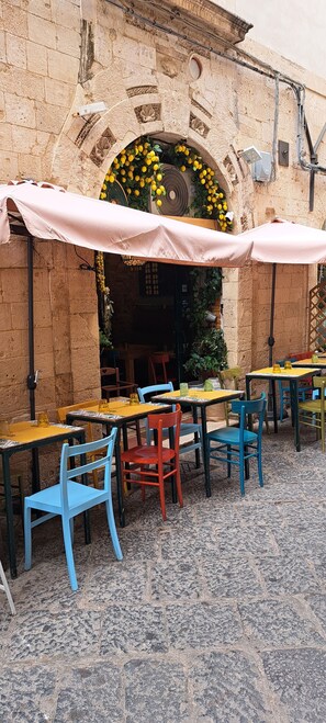 Un café en plein air avec des tables et des chaises, un mur en pierre et une arche décorative.