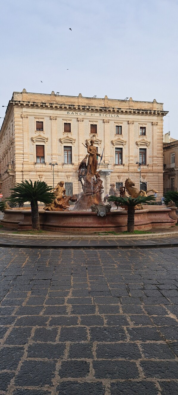 Un bâtiment historique doté d’une fontaine ornée de statues de femmes et de chevaux.