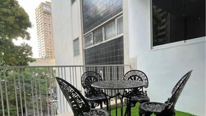 Een balkon met een kleine tafel en stoelen, omgeven door een witte muur en een metalen hekwerk.