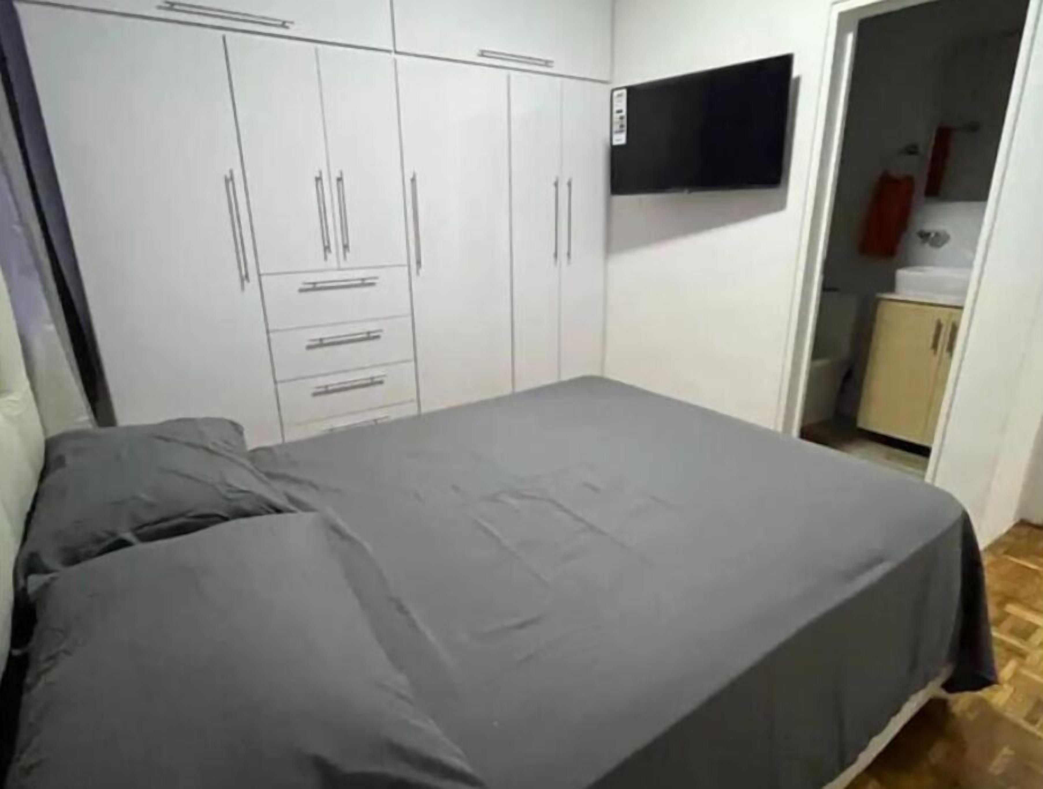 Et soveværelse med seng, garderobe og fjernsyn ophængt på væggen.