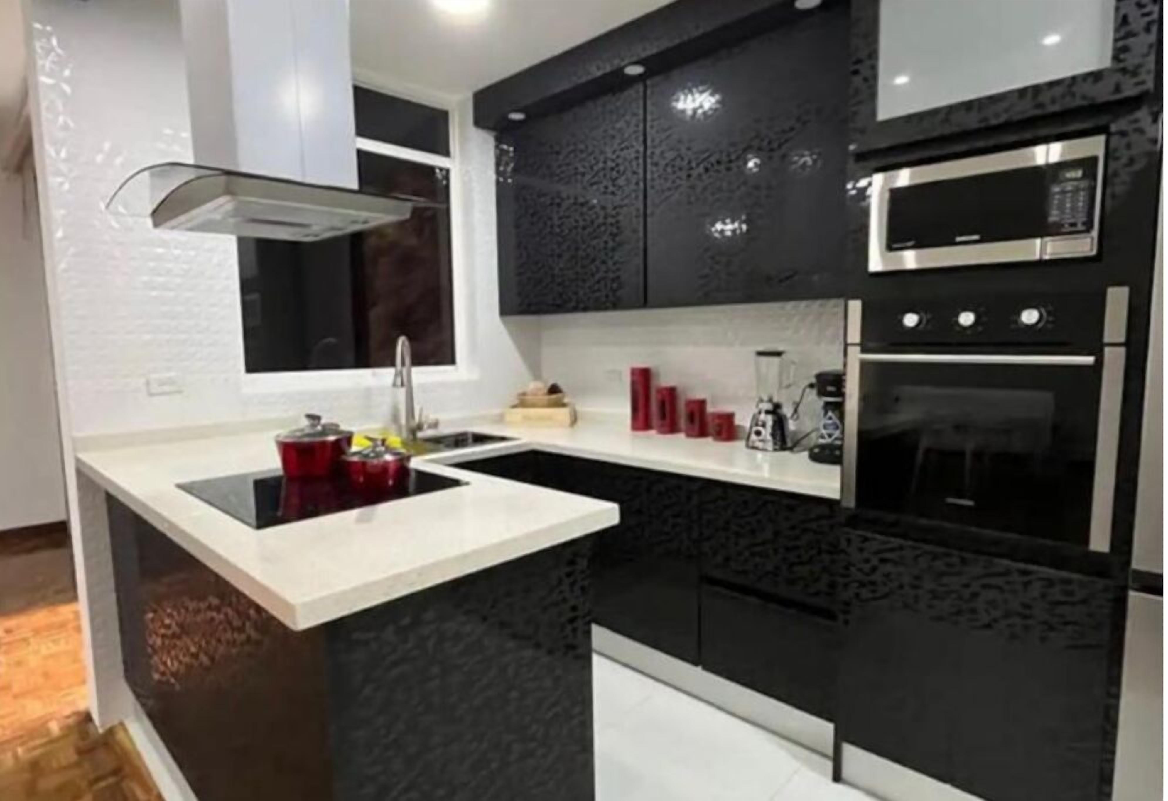 A modern kitchen with black cabinets, a white countertop, a built-in stove, and a microwave.