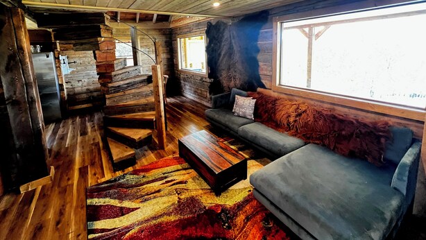 A log cabin interior with a staircase, a sofa, a coffee table, and a large window.