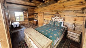 A wooden cabin bedroom with a bed, dresser, vanity, and a window.