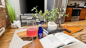 Une table en bois sur laquelle se trouvent un verre contenant une boisson rouge, un livre, une télécommande et une petite plante.