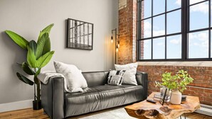 Un salon moderne avec un canapé en cuir, une table basse et une grande fenêtre donnant sur un mur en briques.