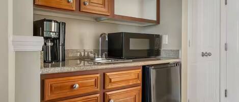 A kitchen with wooden cabinets, a stainless steel dishwasher, a black microwave, and a coffee maker.