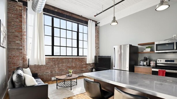 A modern kitchen with a large island, stainless steel appliances, and a brick wall.