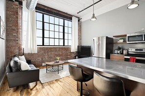 A modern kitchen with a large island, stainless steel appliances, and a brick wall. - Chic Loft in Peoria Warehouse District (Peoria)