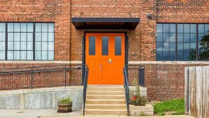 A brick building with a bright orange door, a concrete staircase, and a metal railing.