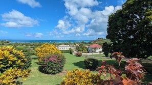 A coastal property with a well-maintained lawn, a variety of colorful plants, and a view of the ocean and hills in the background. - Caribbean Sea View Cottage (St mary's)