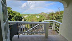 Ein Balkon mit Blick auf eine üppige Landschaft, einen Regenbogen und ferne Hügel.