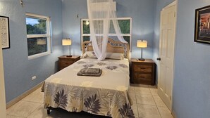 Ein Schlafzimmer mit einem Bett, zwei Nachttischen, einem Fenster, einer Tür und einem Deckenventilator.