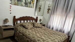 A bedroom with a wooden bed, patterned bedding, a nightstand with a lamp, and a wall-mounted mirror. - Your perfect stay here, with grill, private garage and wifi, centrally located. (Neuquén)