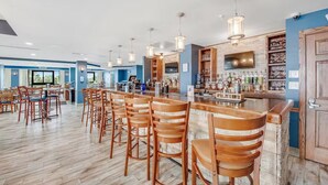 A bar area with wooden chairs and a bar counter, featuring hanging pendant lights and a television screen.
