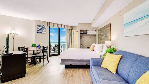 A hotel room with a bed, a sofa, a desk, and a dining area with chairs.