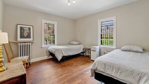 Une chambre avec deux lits, un radiateur, un chauffage d’appoint et une fenêtre donnant sur un espace verdoyant.