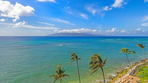 Une plage tropicale aux eaux turquoise et limpides, bordée de palmiers, avec une montagne lointaine se dressant sous un ciel d’un bleu éclatant.