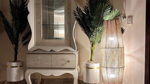 A room with a marble floor, a white vanity with a mirror, two potted plants, and a tall floor lamp.