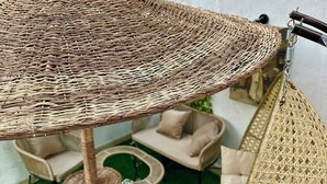 A wicker umbrella and hanging bag in a patio area with a green artificial lawn, beige sofas, and a wicker chair.