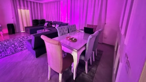 A modern living room with a dining area, featuring a sofa, a dining table with chairs, and a laptop on the table.