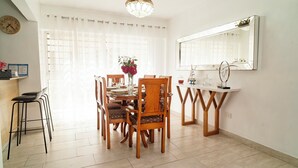 A dining area with a wooden table and chairs, a chandelier, a mirror, and a clock on the wall.