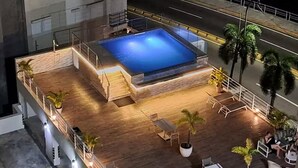 A rooftop pool area with a rectangular pool, seating, and potted plants.