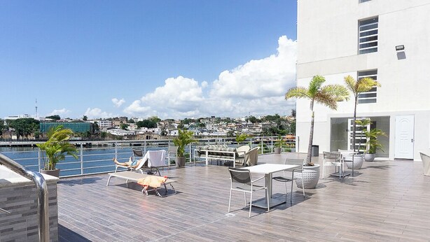 A rooftop terrace with a pool, lounge chairs, and a dining area overlooking a cityscape.