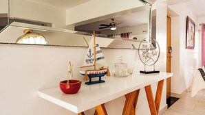 A white console table with a small model sailboat, a red bowl, and a glass container.