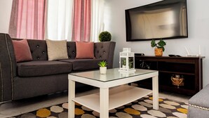 A modern living room with a dark grey sofa, a glass coffee table, a flat-screen TV, and a patterned rug.