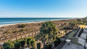 A beach view with a wooden boardwalk, palm trees, and a concrete patio with a table and chairs. - Beachfront Boardwalk Escape (Carolina Beach)