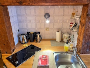 A compact kitchen with a patterned backsplash, a coffee maker, a kettle, a toaster, and a sink.