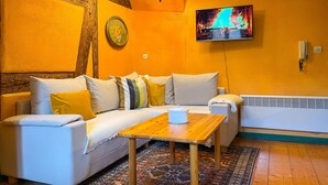 A cozy living room with a sofa, a wooden coffee table, a TV, and a radiator. - La Maison Bleue - Historic house in the heart of Riquewihr. "Le Renard" 2-guest apartment (Riquewihr)