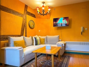 A cozy living room with a sofa, a wooden coffee table, a TV, and a radiator. - La Maison Bleue - Historic house in the heart of Riquewihr. "Le Renard" 2-guest apartment (Riquewihr)