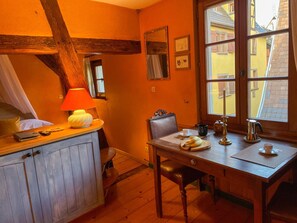 A cozy room with a wooden table, a chair, a lamp, and a window with a view of buildings outside. - La Maison Bleue - Historic house in the heart of Riquewihr. "Le Renard" 2 guest flat (Riquewihr)