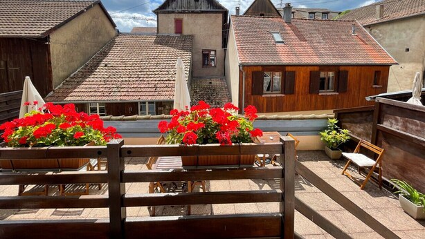A courtyard with wooden benches, red flowers, and traditional buildings with tiled roofs. - La Maison Bleue - Historic house in the heart of Riquewihr. "Le Renard" 2-guest apartment (Riquewihr)