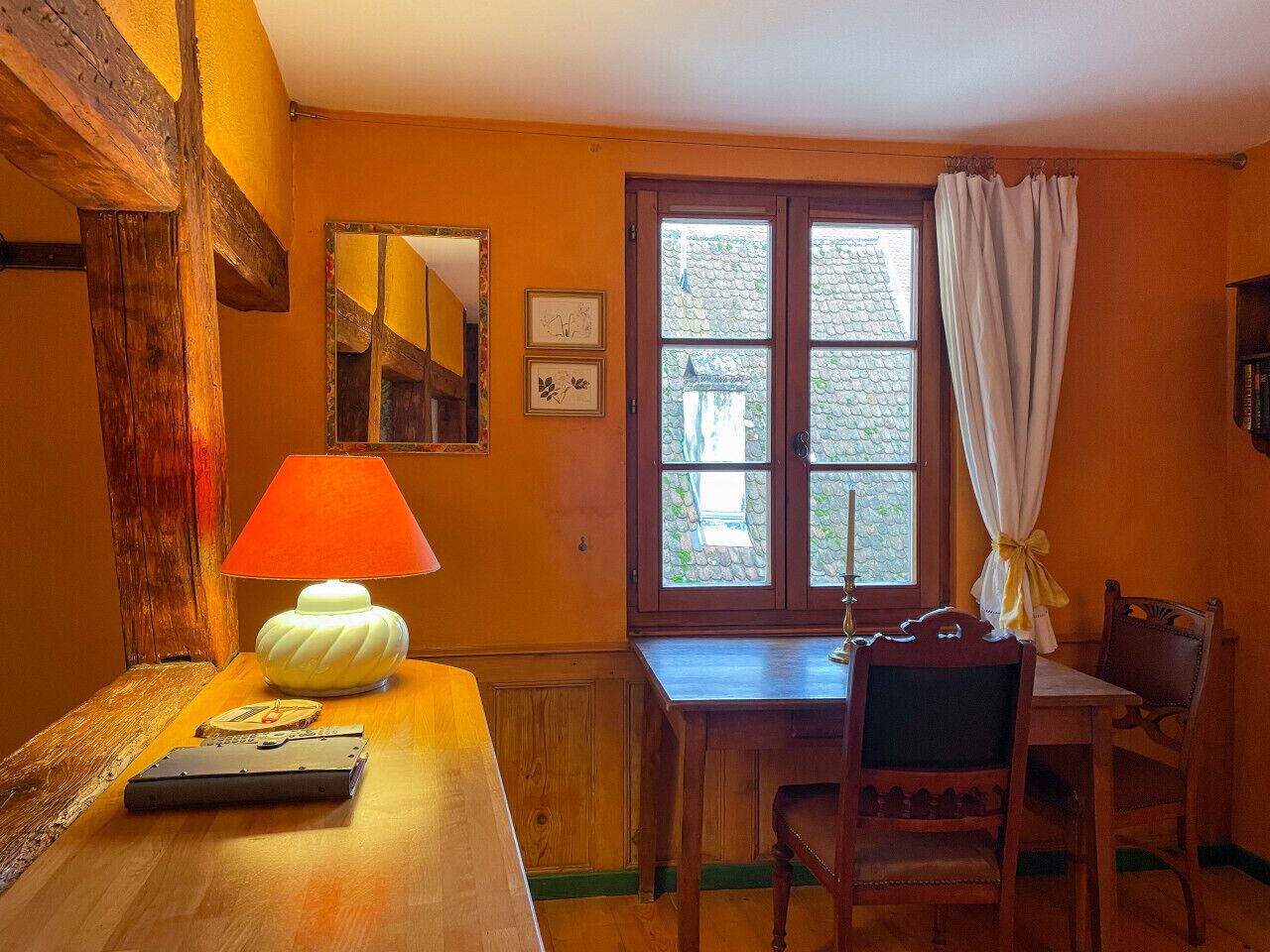 A cozy room with a wooden table, a lamp, a chair, and a window with curtains.
