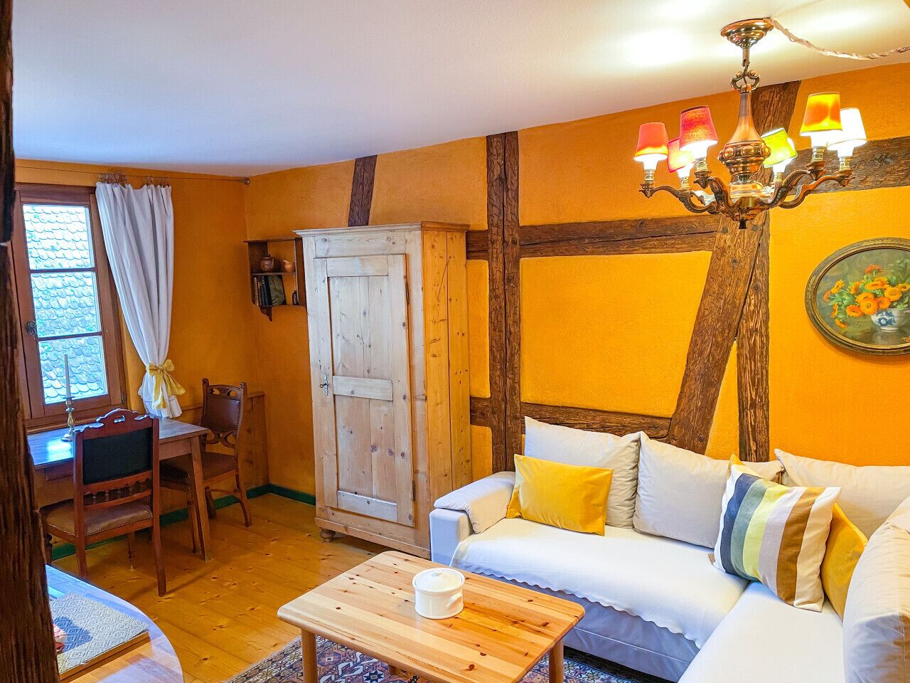 Une pièce chaleureuse avec une table en bois, un canapé blanc agrémenté de coussins jaunes, une armoire en bois et un lustre.