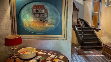 Un hall d’hôtel avec un tableau encadré représentant une maison, un escalier et une table ronde sur laquelle sont disposées des brochures.