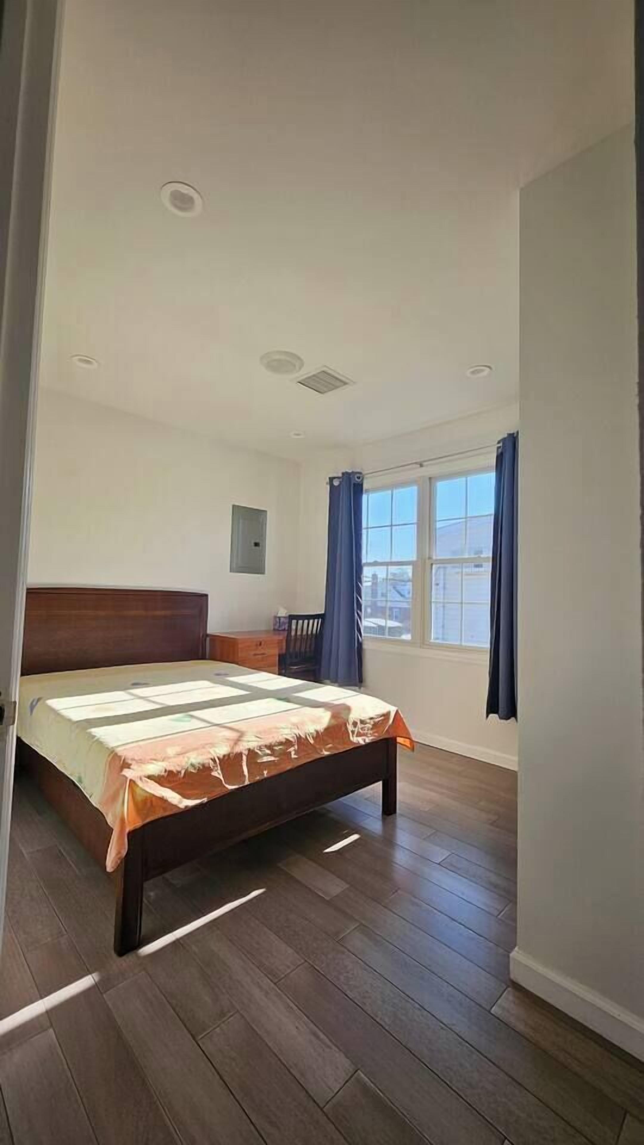 A bedroom with a bed, a window with curtains, and a wooden floor.