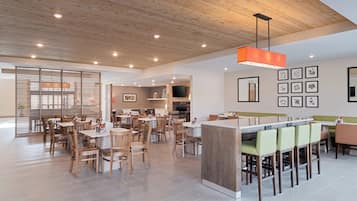 A spacious dining area with wooden tables and chairs, a central island with seating, and a modern ceiling design.